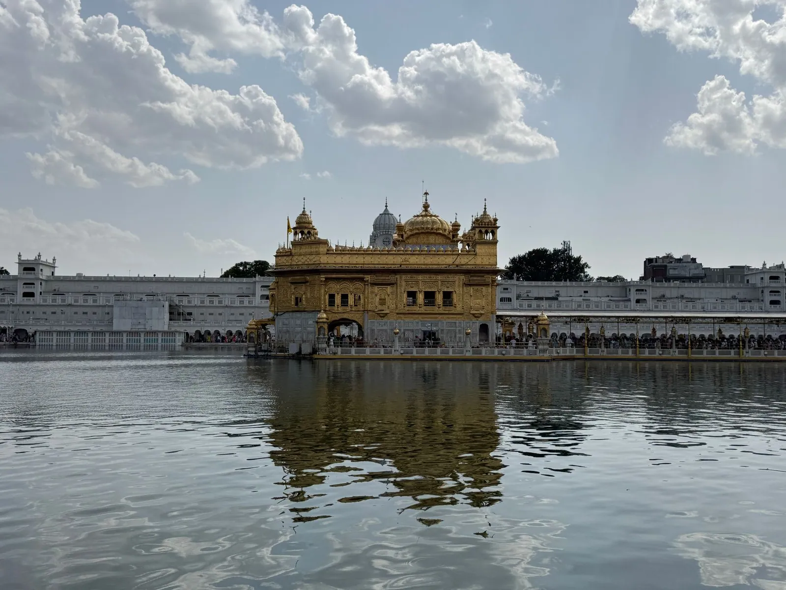 Stunning view of the Golden Temple reflecting in water under a bright, cloudy sky in Amritsar, India
