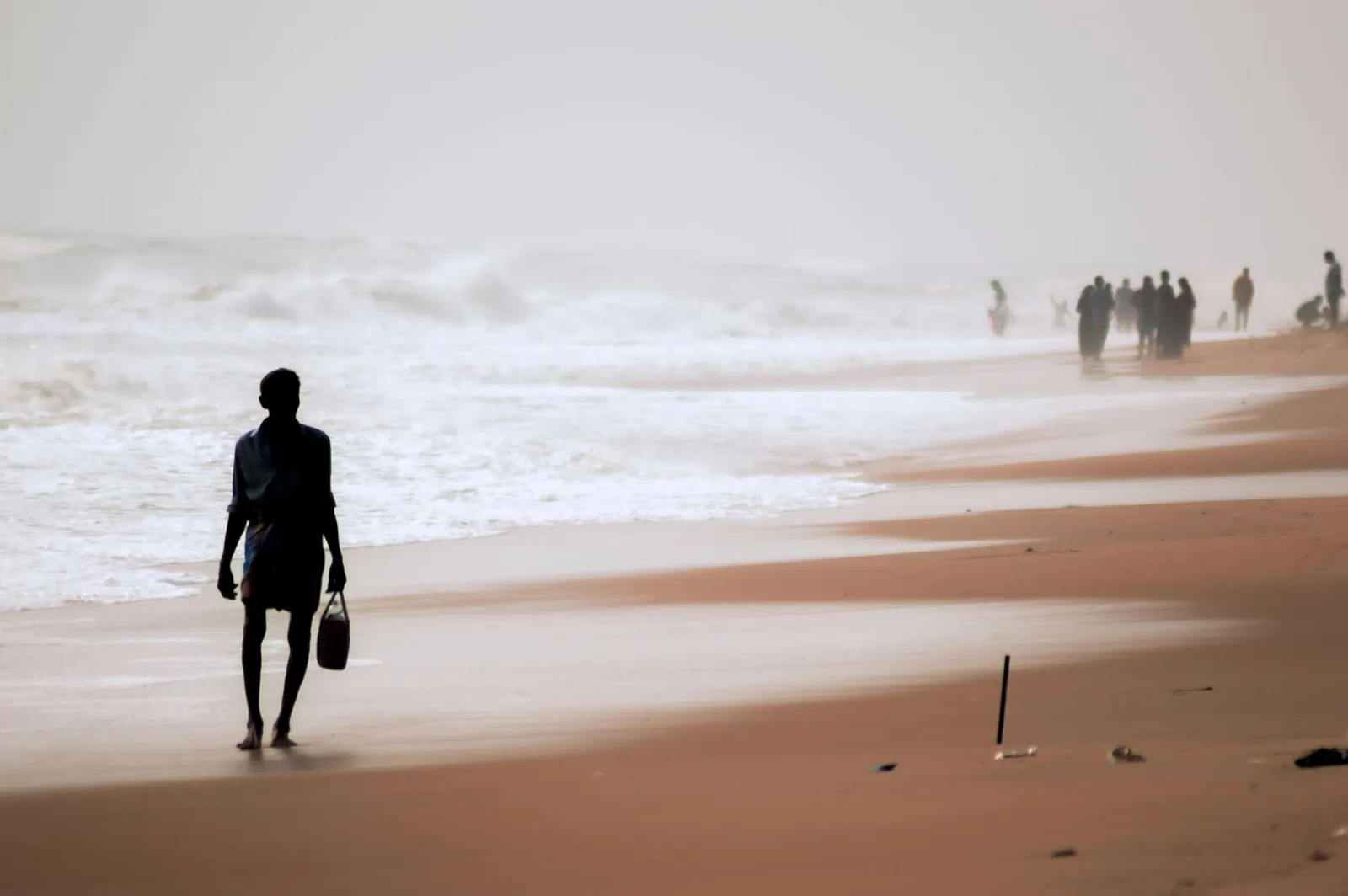 A silhouette of a man walking barefoot on the sandy beach of Chennai, India with ocean waves in the background.