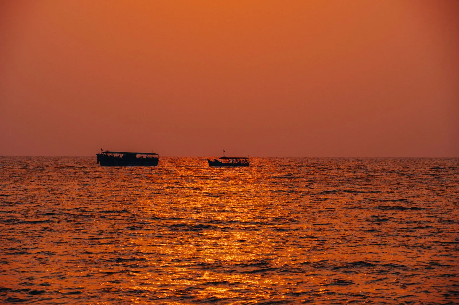 Peaceful seascape at sunset with two boats silhouetted against an orange sky in India