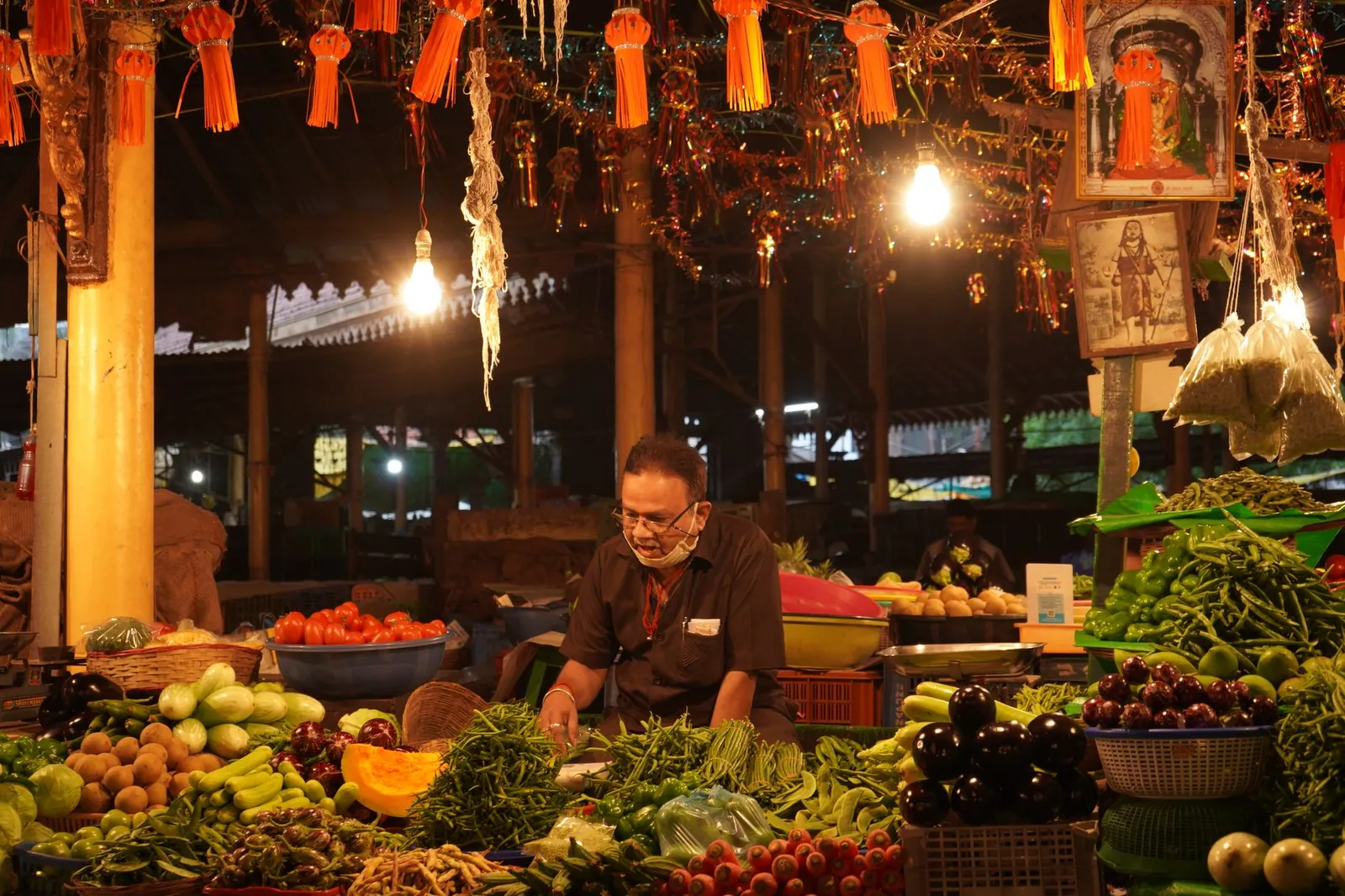 An Indian vendor selling fresh vegetables in a lively bazaar at night.