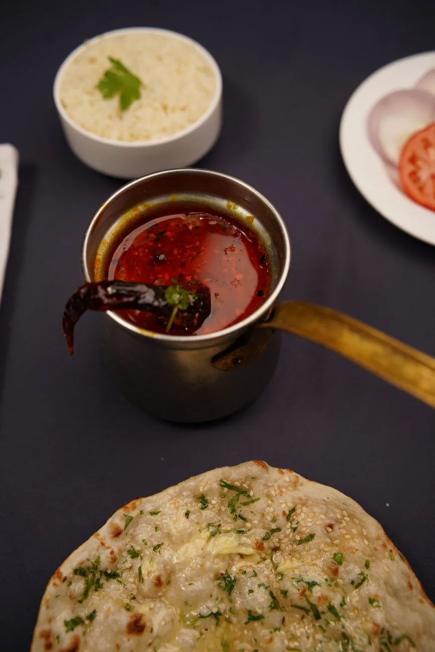 Delicious spread of Indian food including spicy sauce pot, garlic naan, rice, and salad.