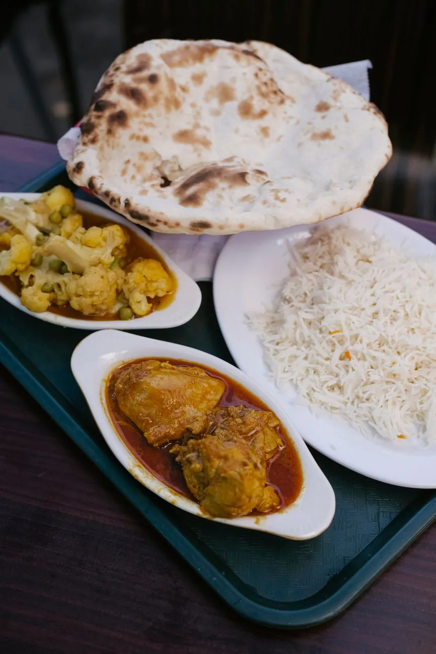 From above of tasty Indian food consisting of curry roti bread rice and stew vegetables on tray