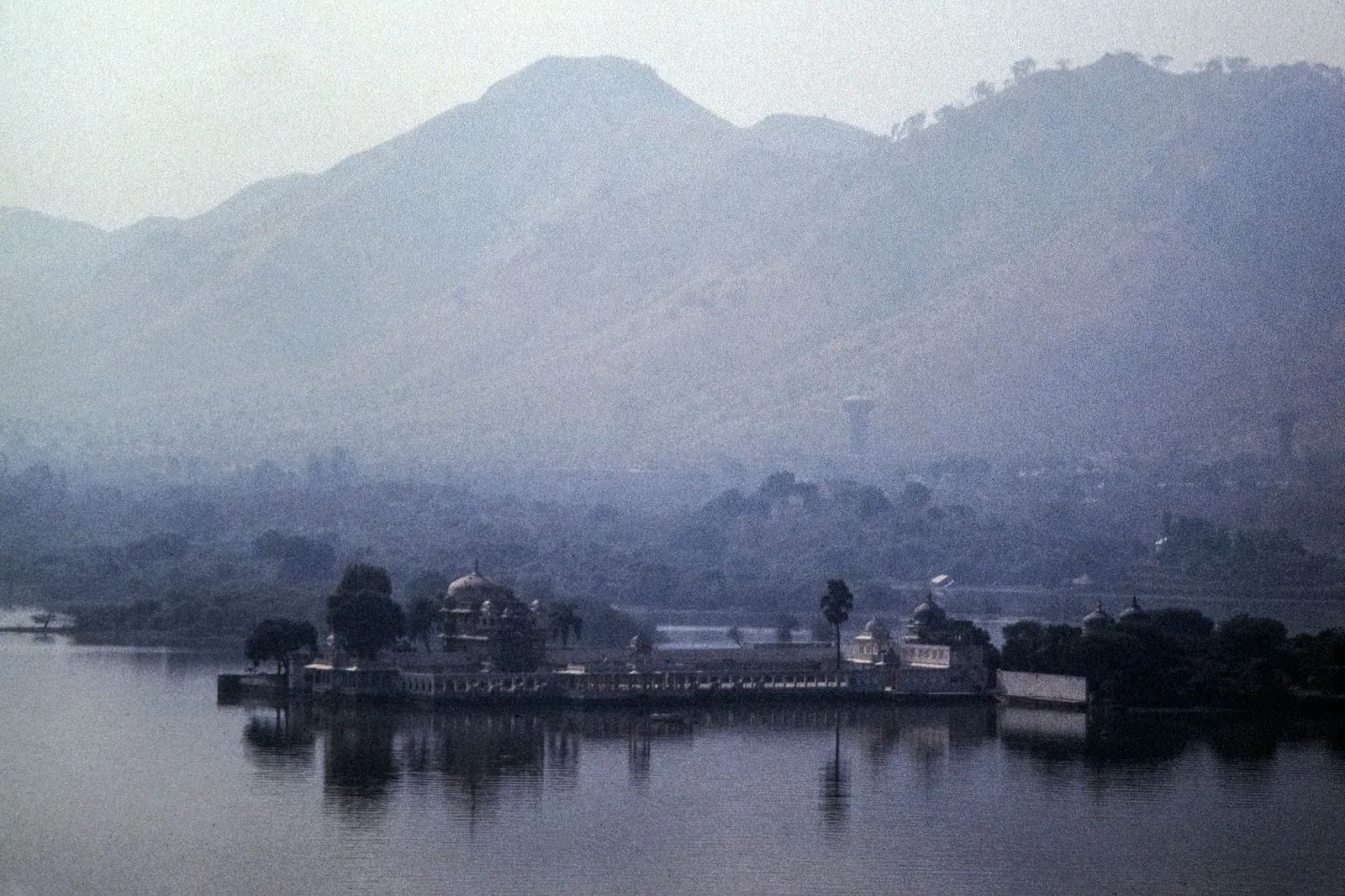 A serene landscape of a lake and hills in Udaipur, India, in mist