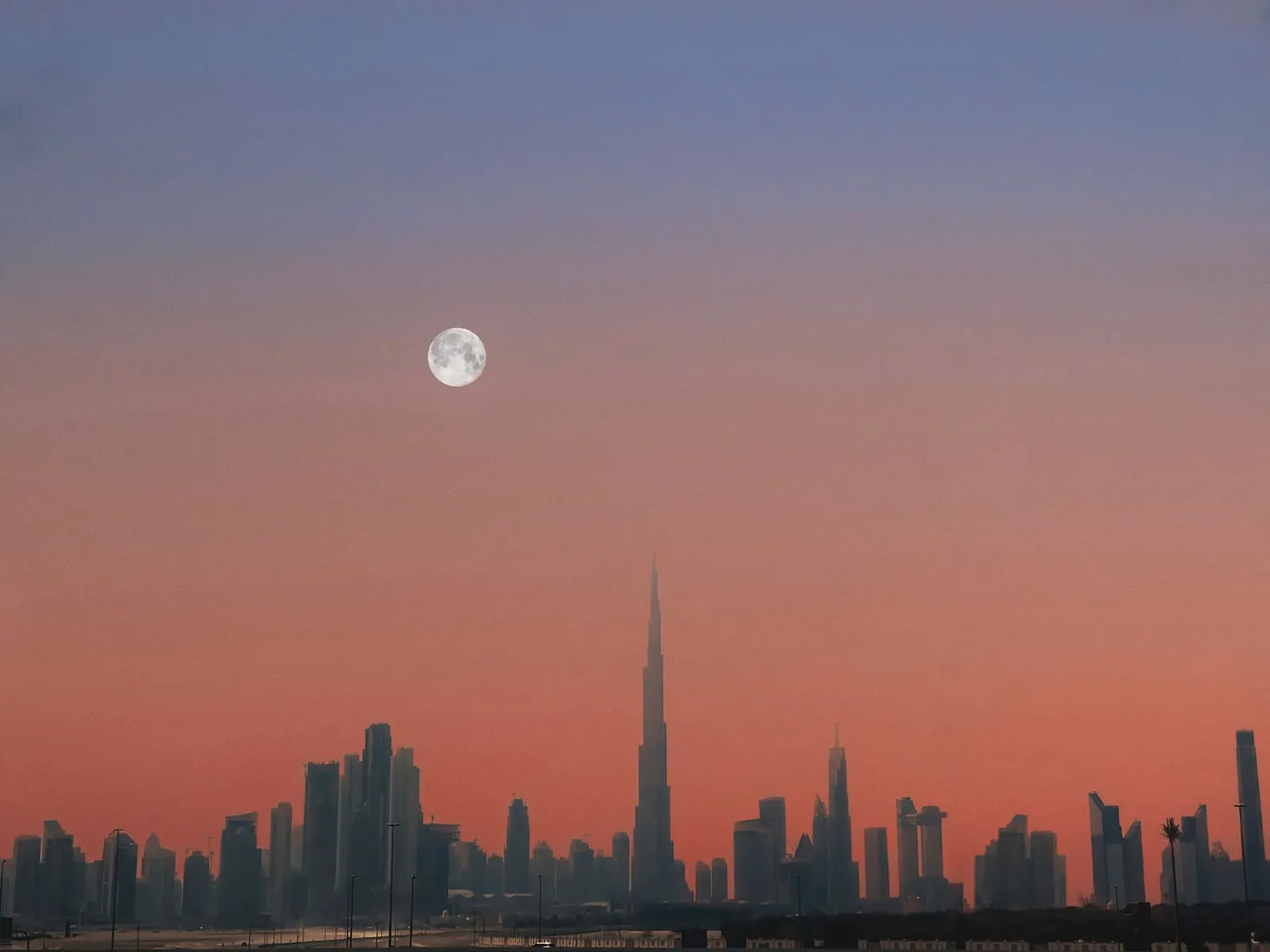 Dubai skyline with the Burj Khalifa at sunset and a full moon in the sky