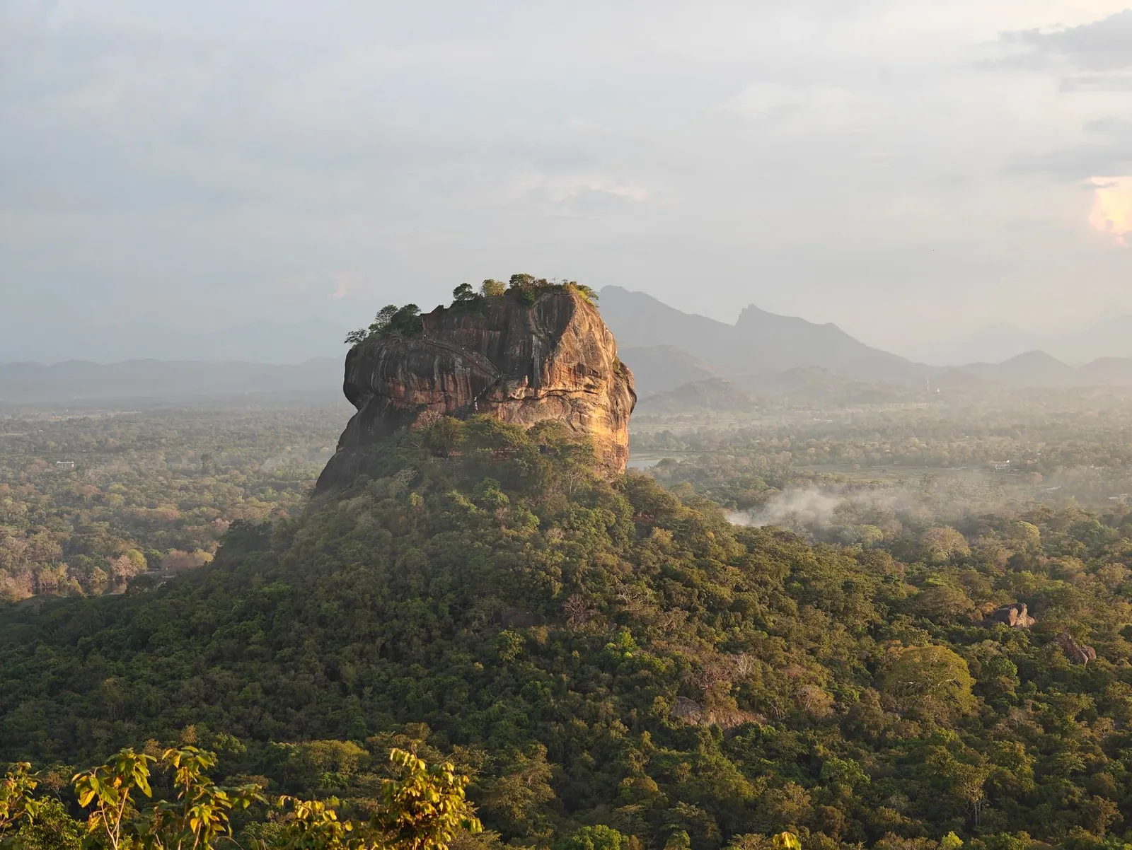 Sigiriya Rock amidst lush forests under a cloudy sky in Sri Lanka