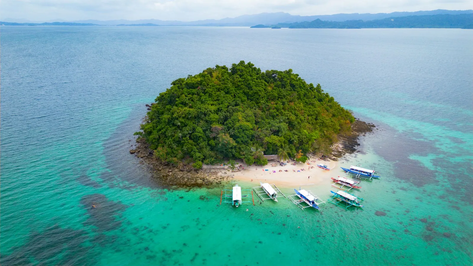 An aerial view of a lush island surrounded by turquoise waters in the Philippines