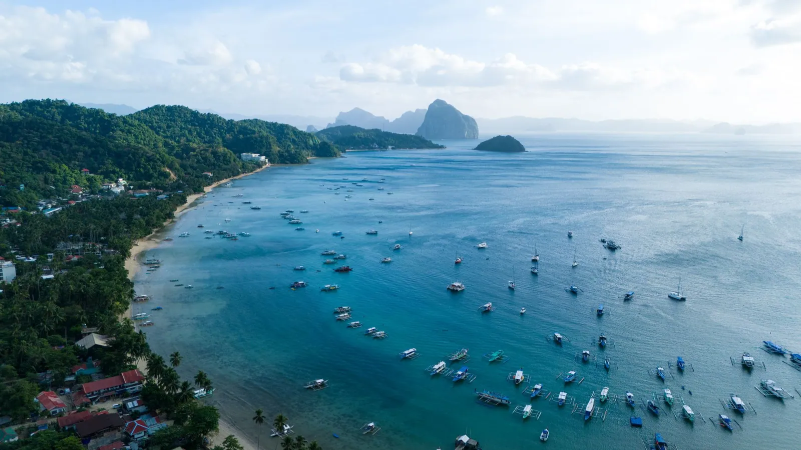 Stunning aerial view of El Nido's vibrant blue bay with lush greenery and boats, capturing the essence of the Philippines' natural beauty.