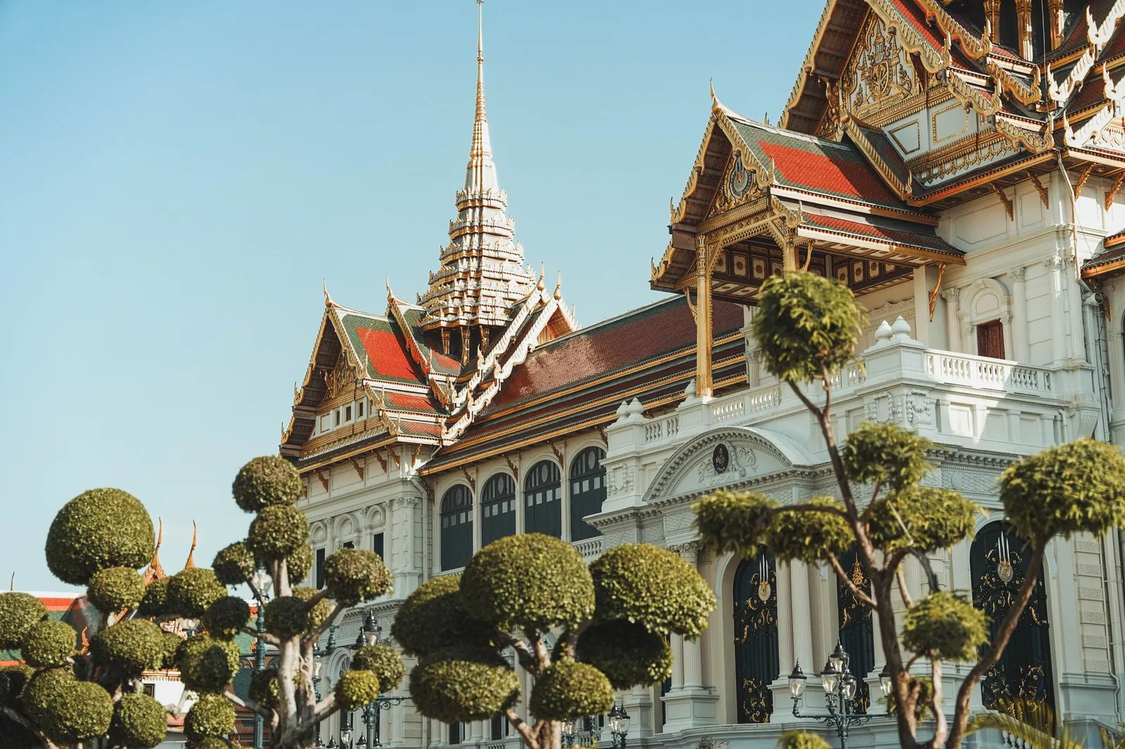 Stunning view of the Grand Palace's ornate architecture with trimmed trees in Bangkok, Thailand