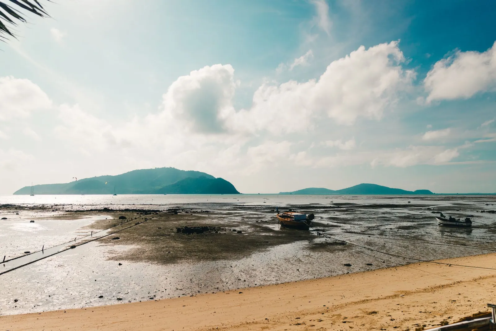 A tranquil beach in Phuket, Thailand, with boats and mountains behind