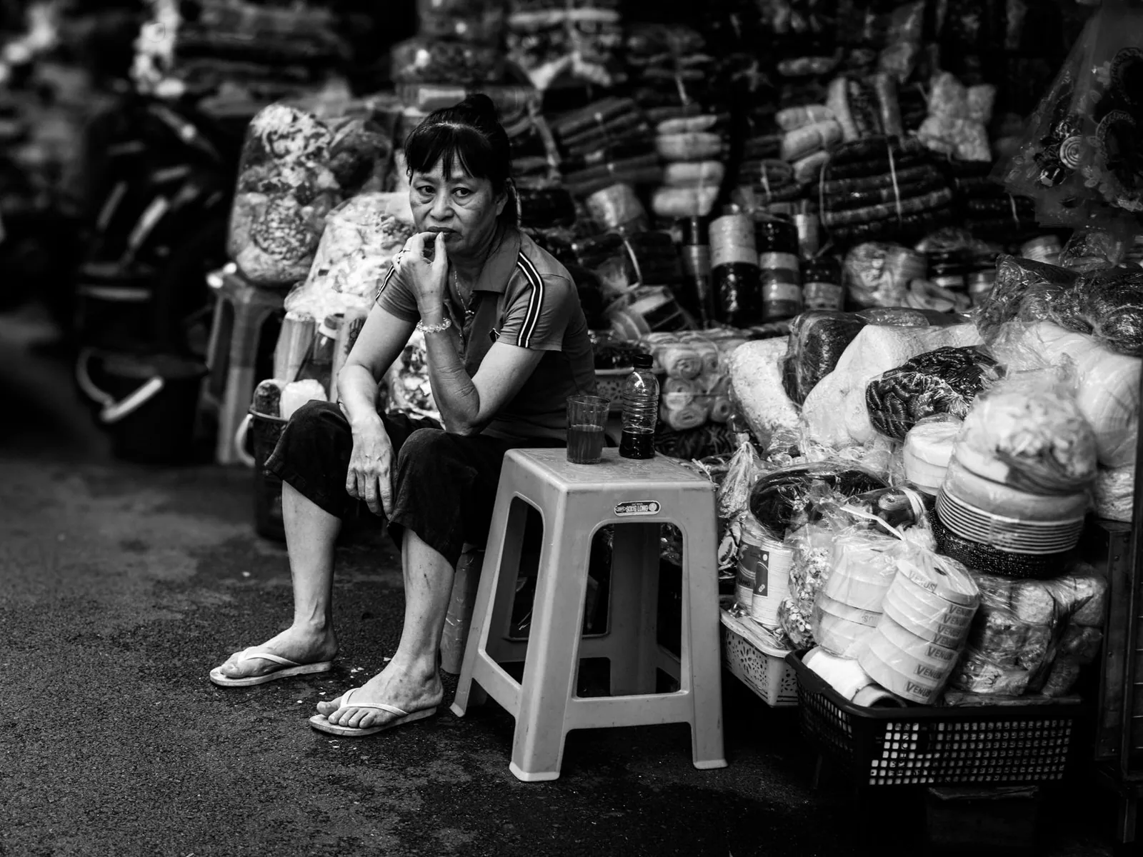A street vendor sitting among goods in a Hanoi market, Vietnam