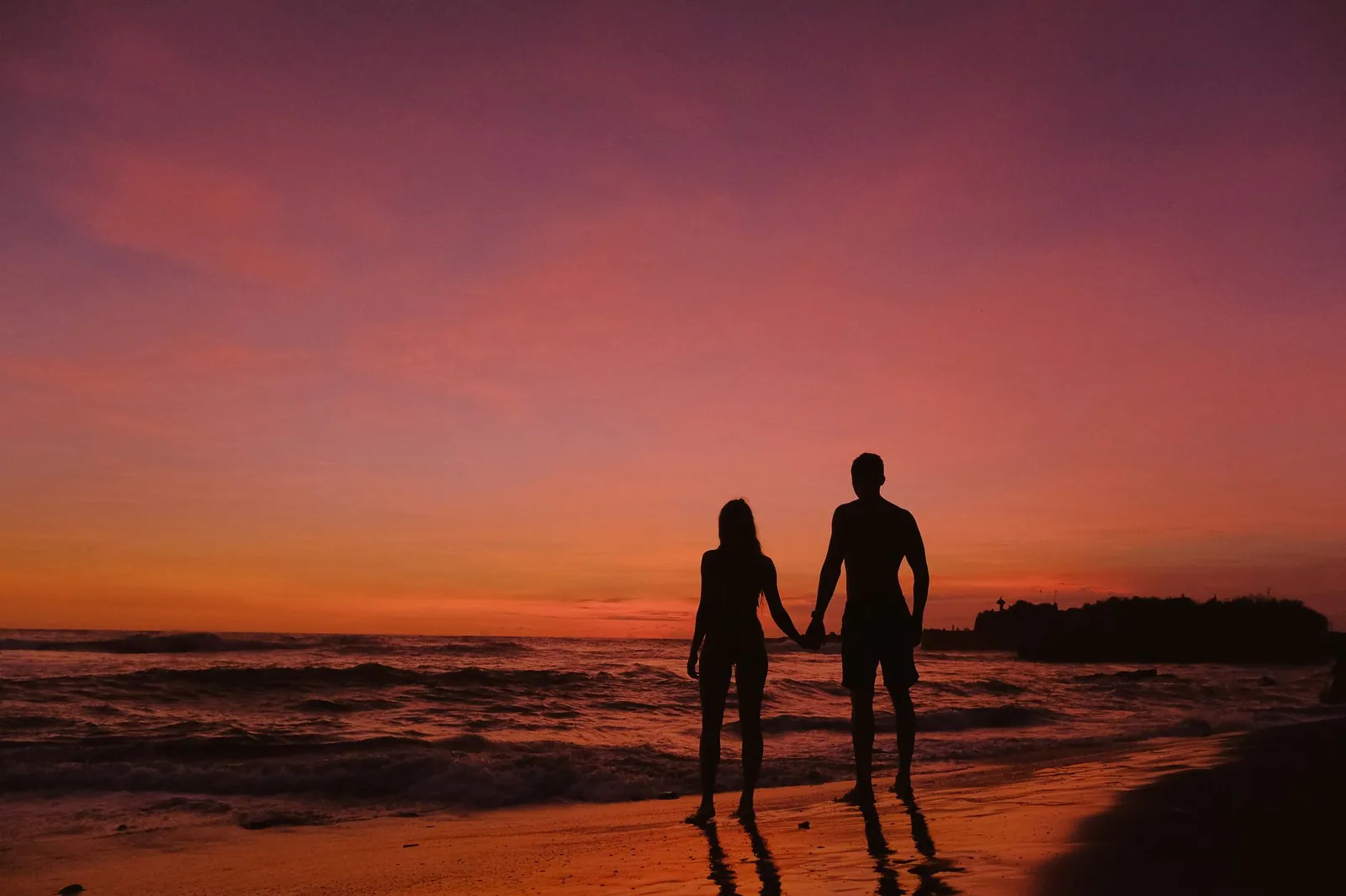 Silhouette of a couple holding hands on the beach at sunset, evoking romance and calm.
