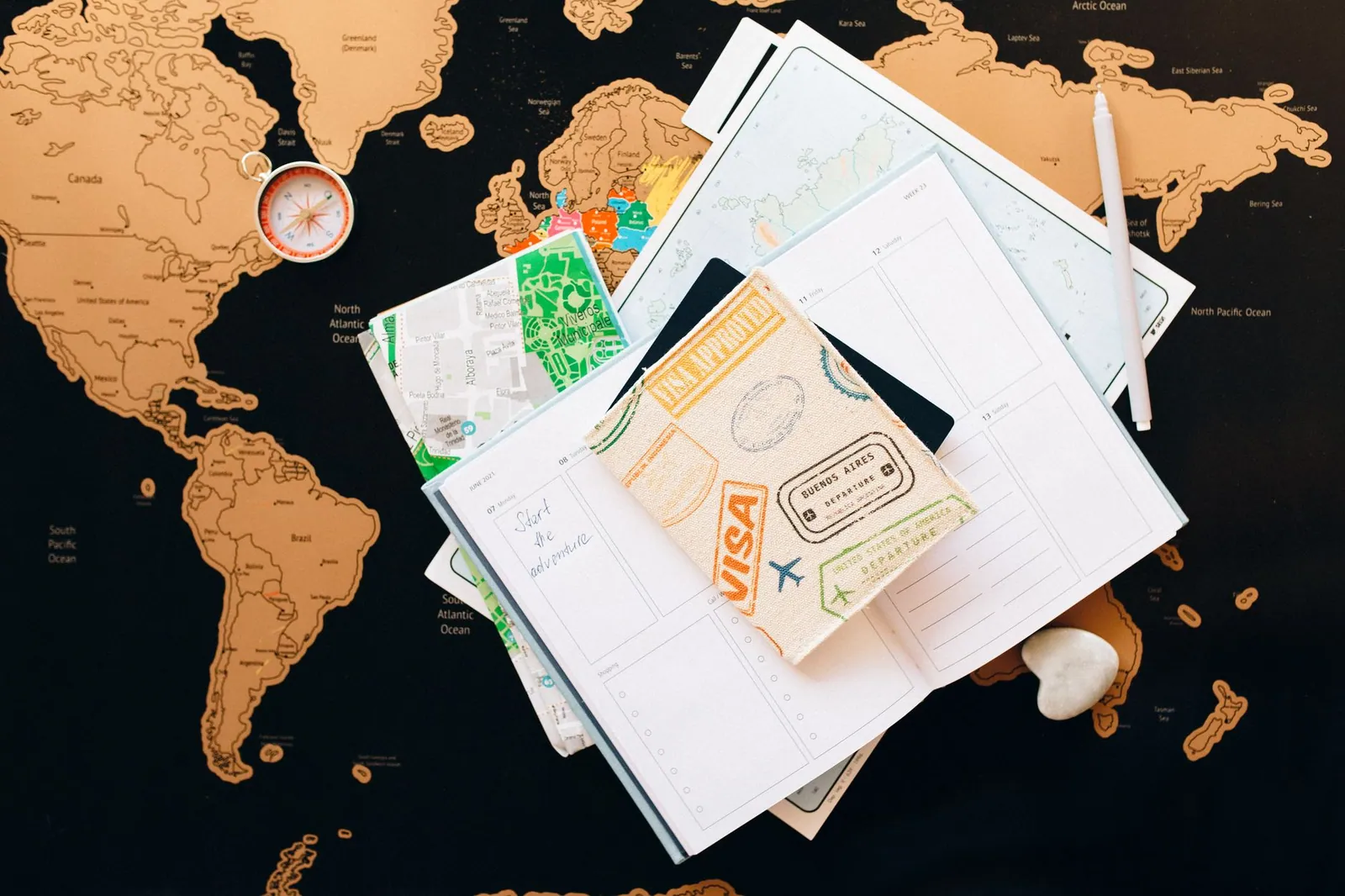 A flat lay of travel planning items including a compass, notebook and guide on a map