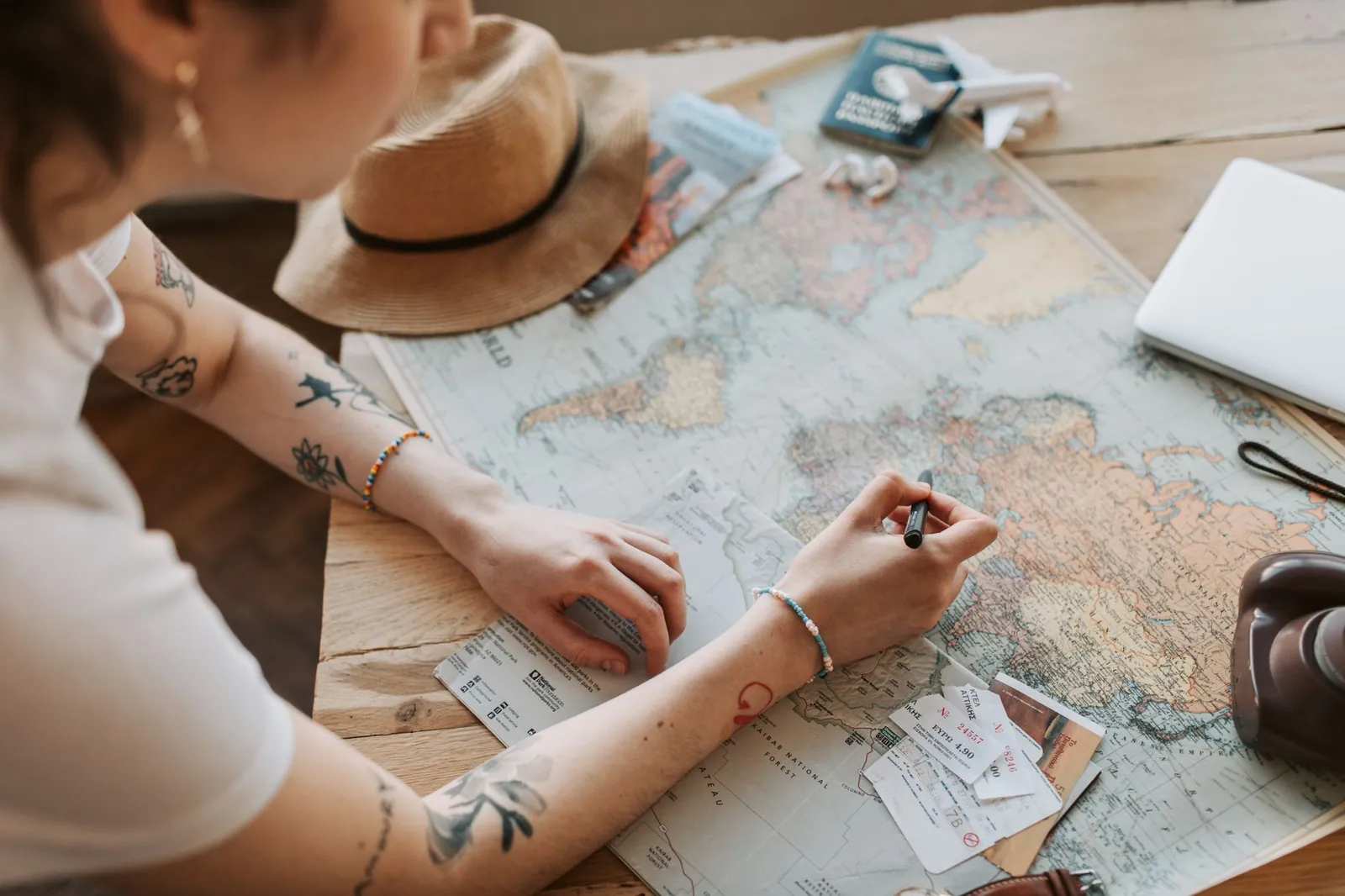 Person planning a journey with a map, passport and travel essentials on a wooden table