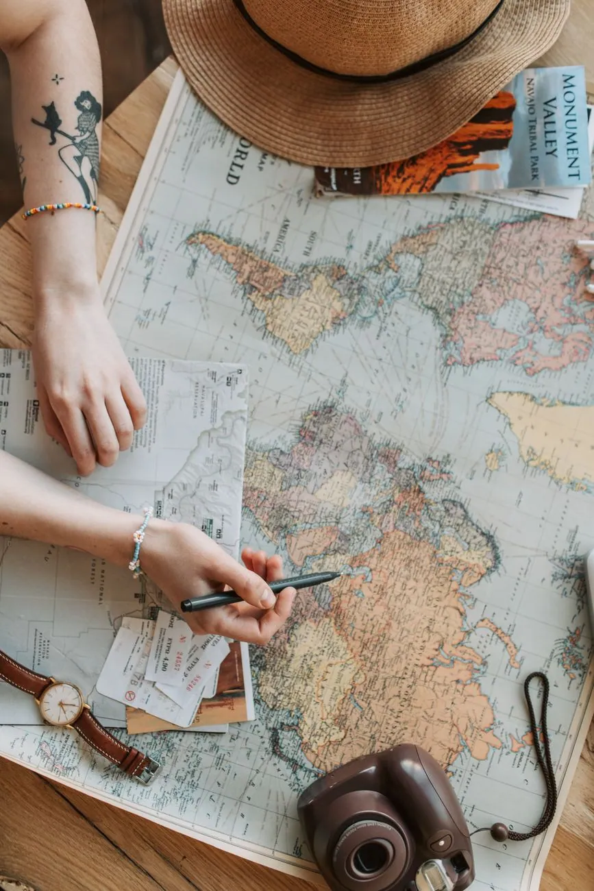 Person planning a journey with a world map, camera and travel guide on a wooden table