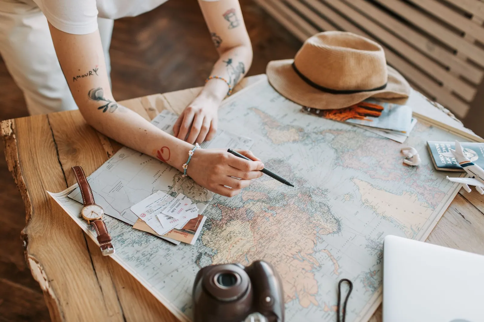 A traveller planning a trip with a world map, passports and travel essentials on a wooden table